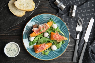 Photo of Flat lay composition of fresh melon with prosciutto, mozzarella and arugula on black wooden table