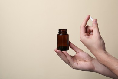 Man holding pill and bottle on beige background, closeup. Space for text