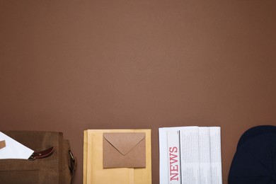 Photo of Postman hat, bag, newspapers and mails on brown background, flat lay. Space for text