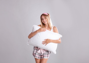 Photo of Young woman in pajamas embracing pillow on gray background