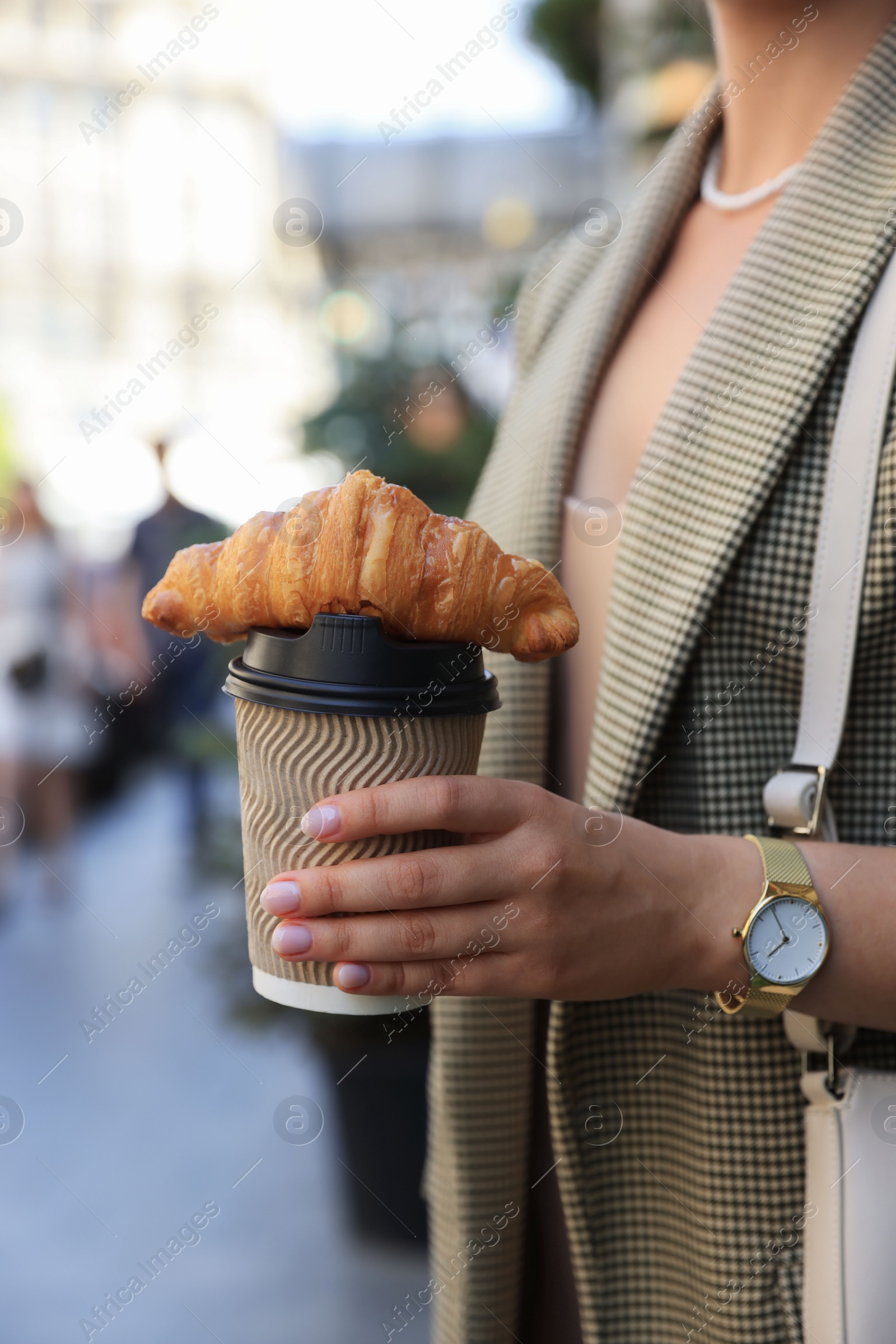 Photo of Woman holding tasty croissant and cup of coffee outdoors, closeup