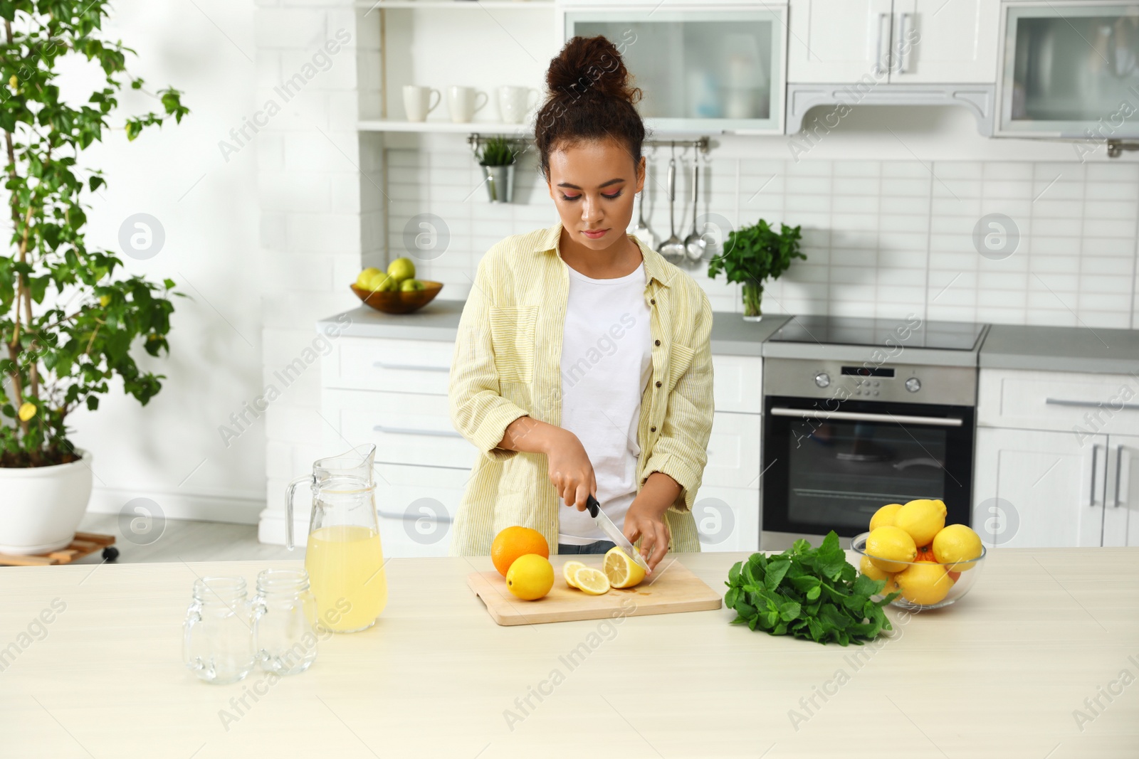 Photo of African-American woman cutting fruits for natural lemonade in kitchen. Detox drink
