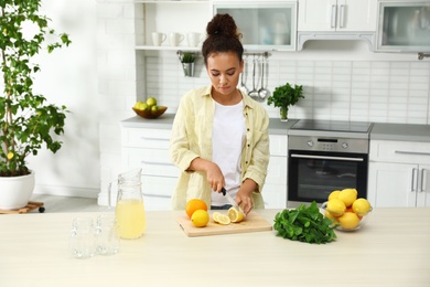 African-American woman cutting fruits for natural lemonade in kitchen. Detox drink