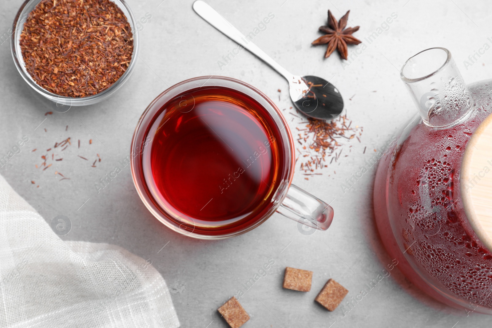 Photo of Freshly brewed rooibos tea, scattered dry leaves and spices on grey table, flat lay