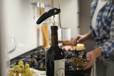 Wine bottle with corkscrew, closeup. Woman in kitchen, selective focus