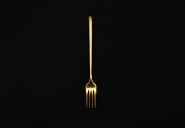 Photo of Shiny gold fork on black background, top view