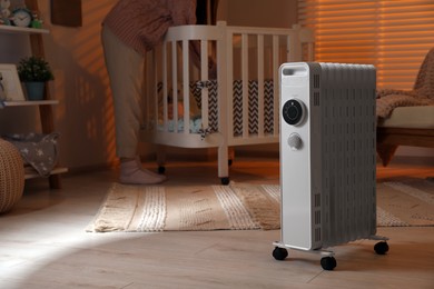 Photo of Woman near crib and modern portable electric heater indoors, closeup. Space for text