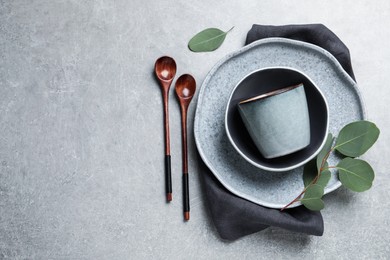 Set of dishware with eucalyptus leaves and napkin on grey table, flat lay. Space for text