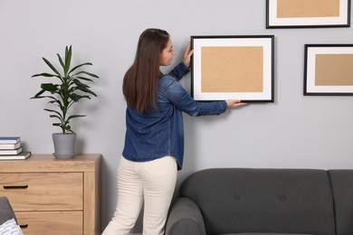 Woman hanging picture frame on gray wall at home