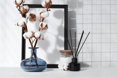 Photo of Reed diffuser, candle and cotton branches with fluffy flowers on white wooden table indoors. Space for text