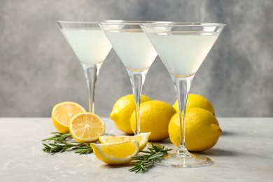 Photo of Martini glasses of refreshing cocktail, lemon and rosemary on light grey textured table
