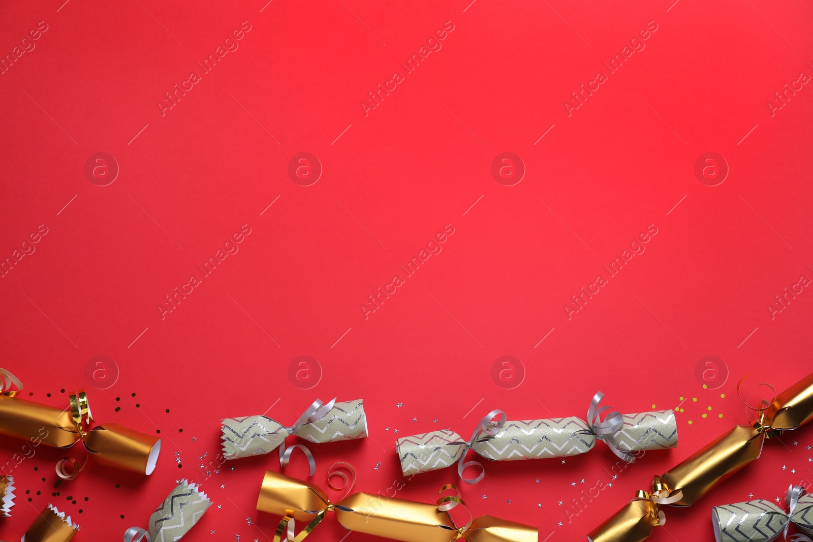 Photo of Open and closed Christmas crackers with shiny confetti on red background, flat lay. Space for text