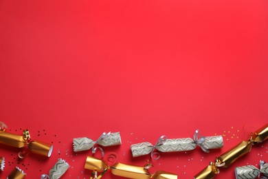 Open and closed Christmas crackers with shiny confetti on red background, flat lay. Space for text