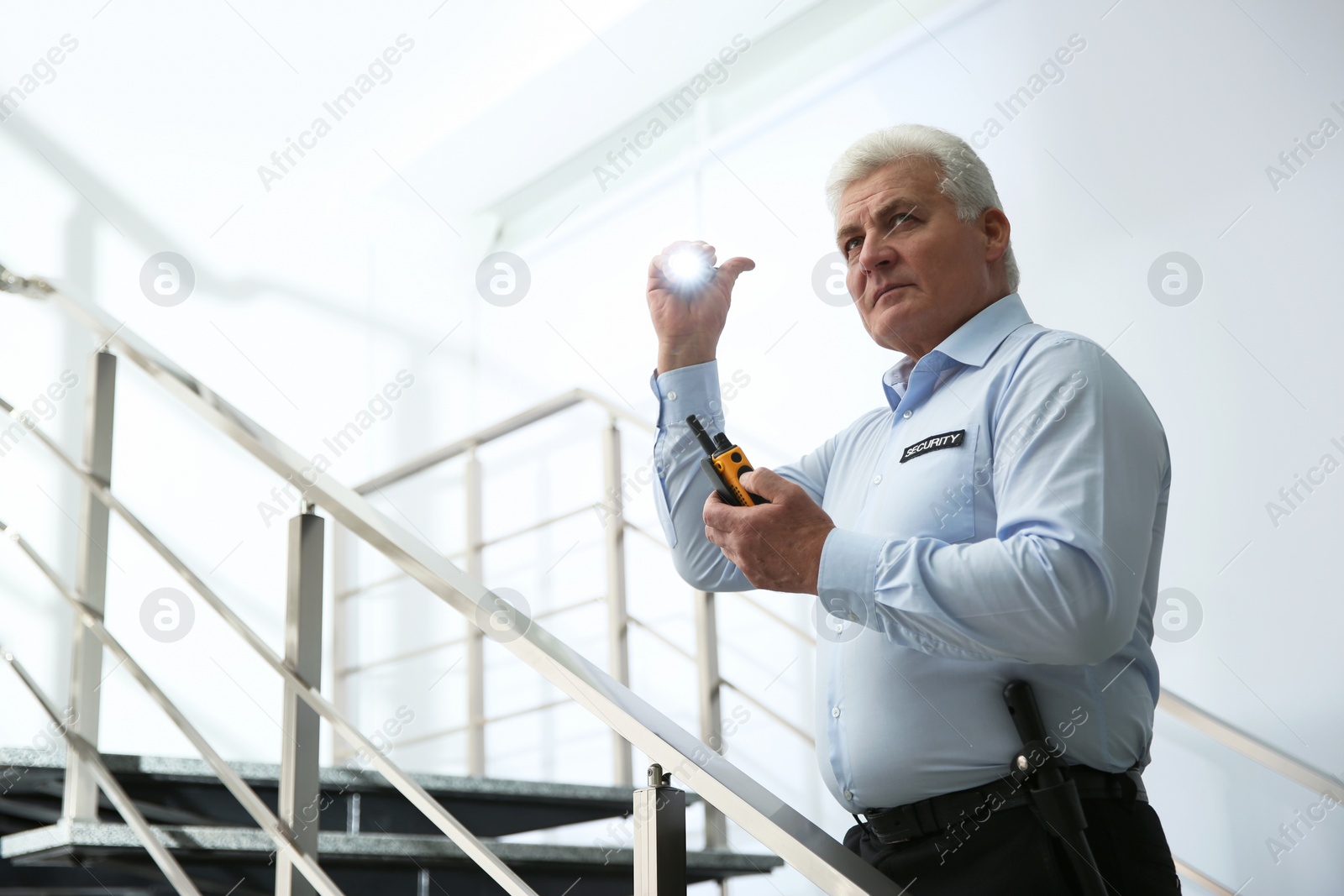 Photo of Professional security guard with portable radio set and flashlight on stairs indoors