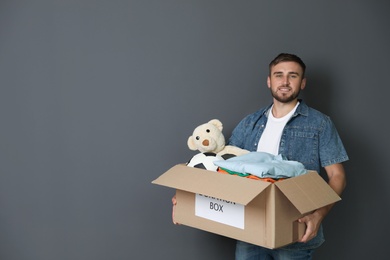 Young man holding box with donations on grey background. Space for text