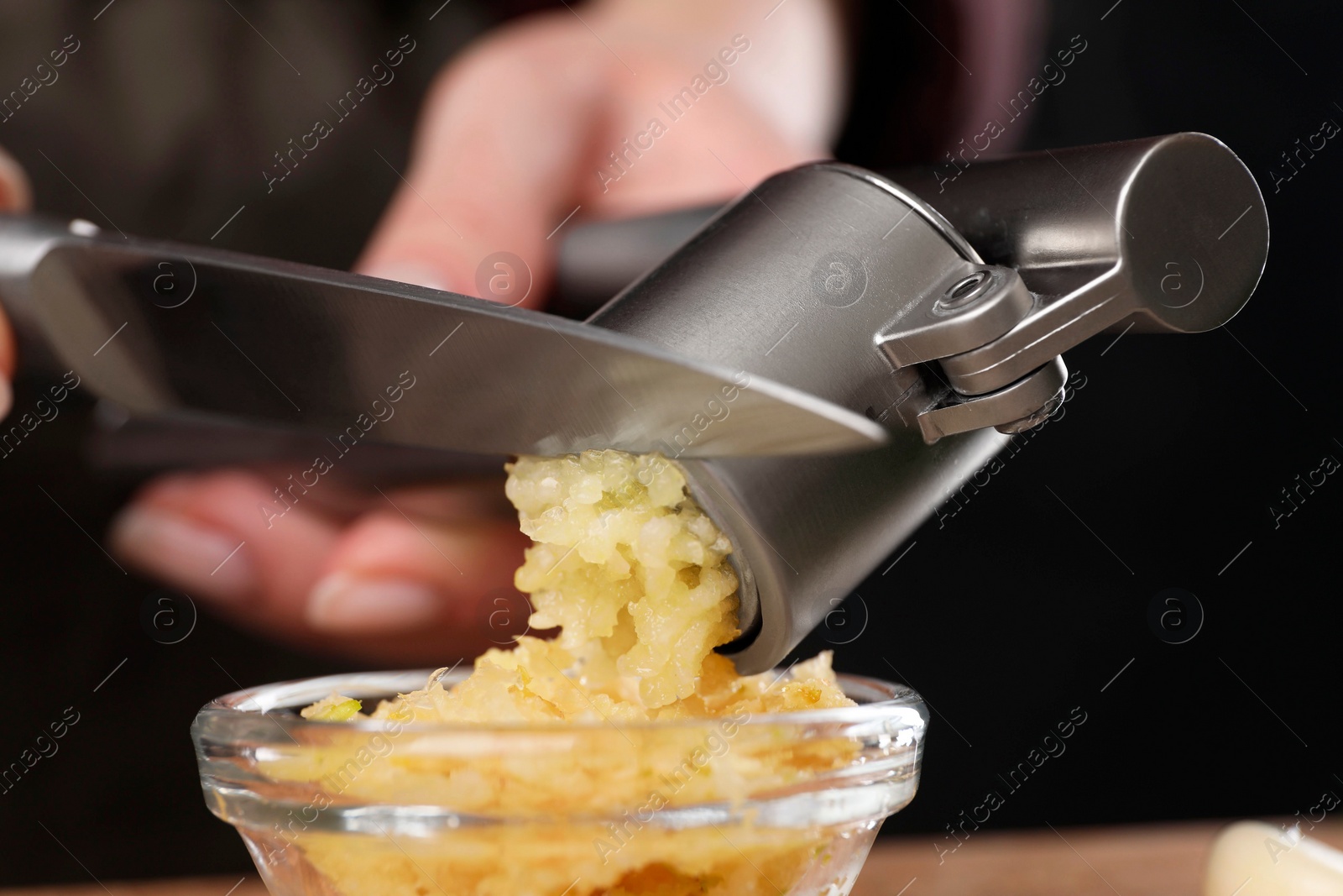 Photo of Woman squeezing garlic with press on blurred background, closeup