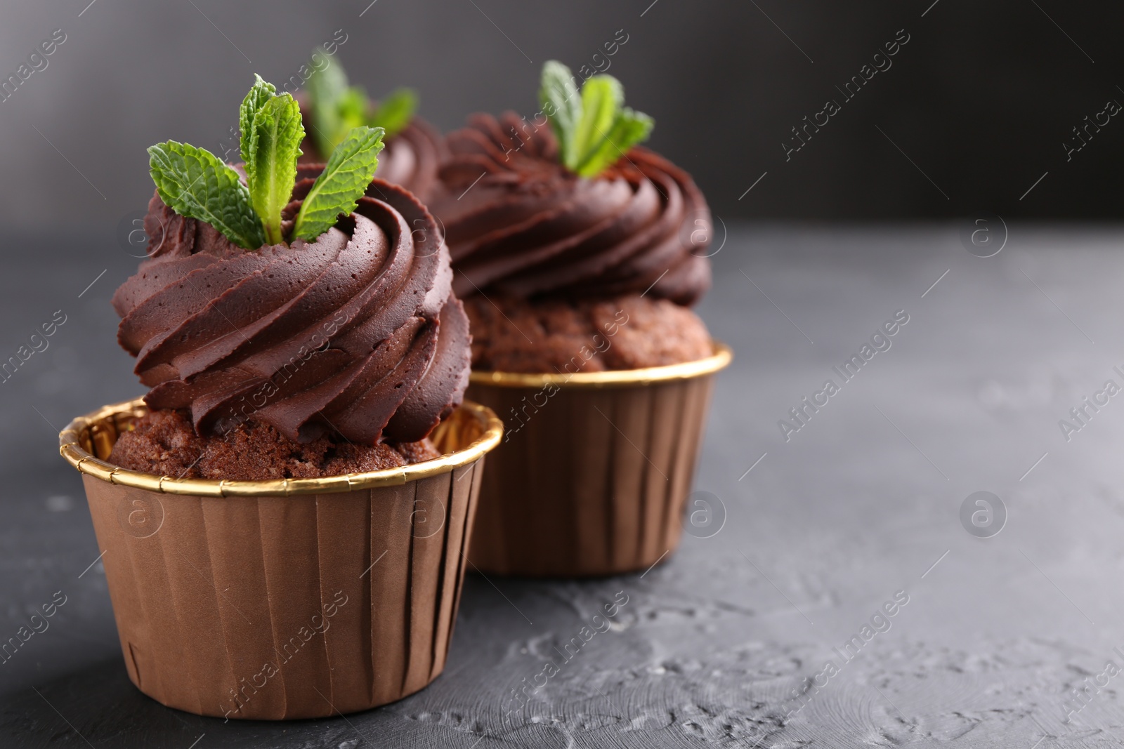 Photo of Delicious chocolate cupcakes with mint on black textured table, closeup. Space for text