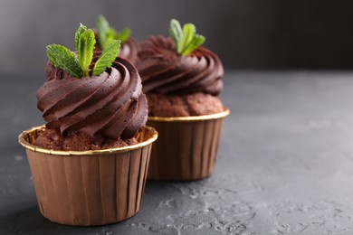 Photo of Delicious chocolate cupcakes with mint on black textured table, closeup. Space for text