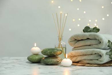 Photo of Spa composition. Towels, stones, reed air freshener and burning candles on white marble table, space for text