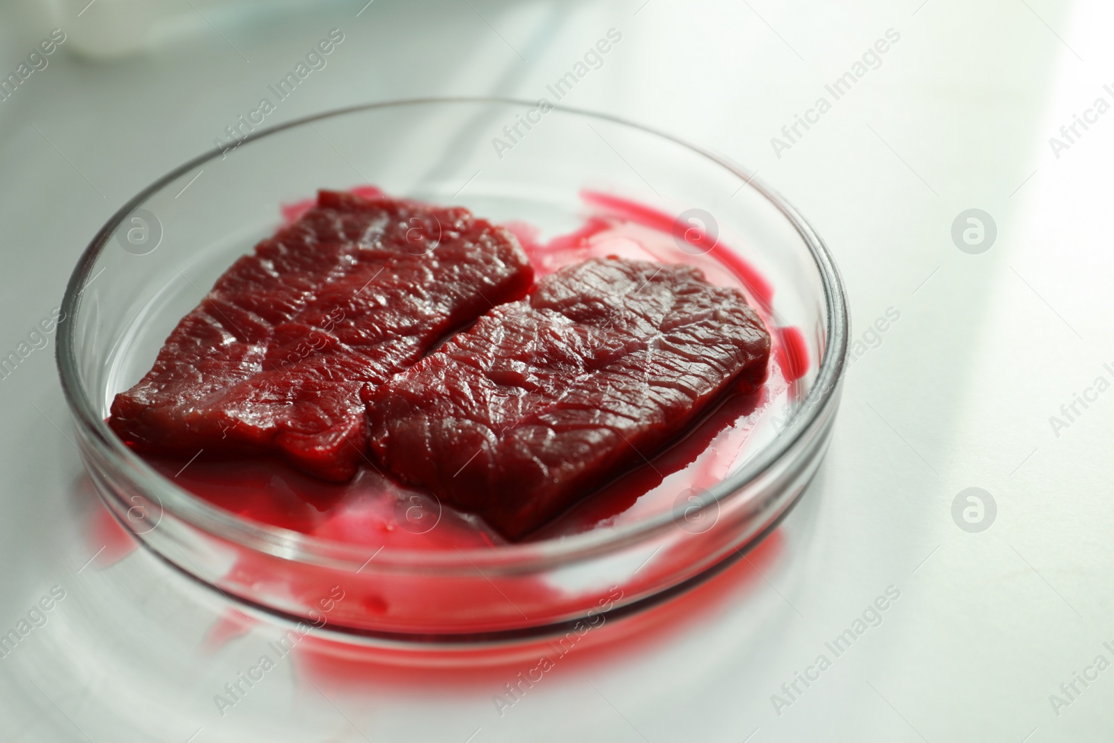 Photo of Petri dish with pieces of raw cultured meat on white table, closeup