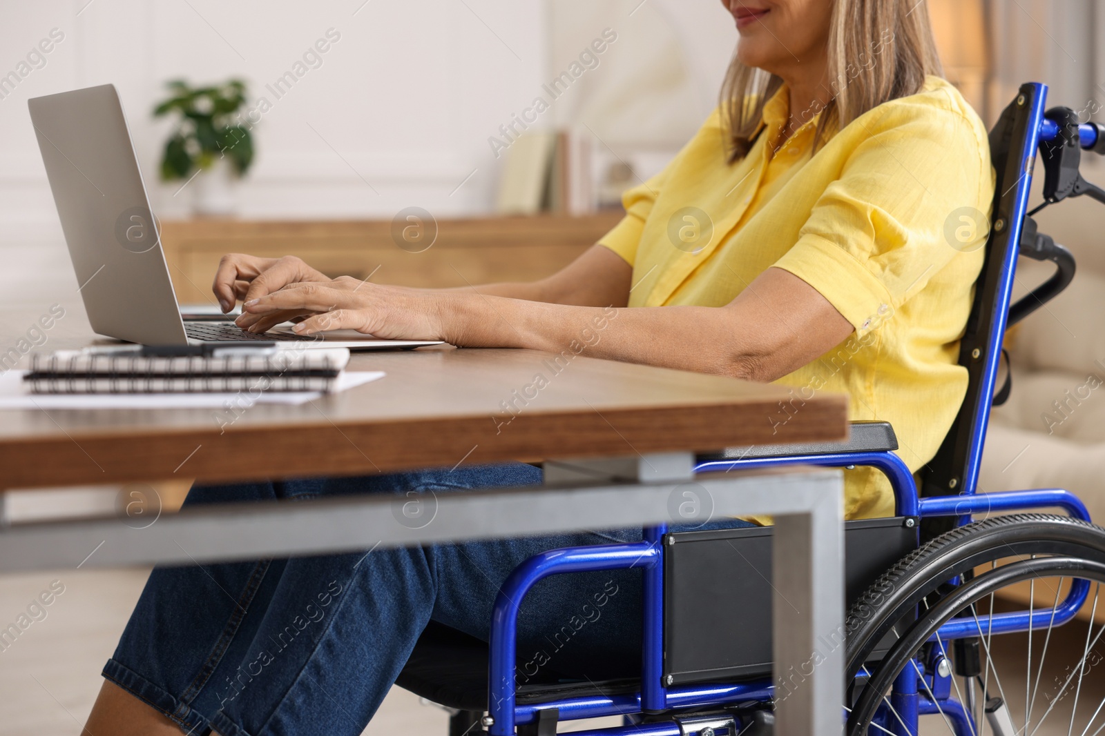 Photo of Woman in wheelchair using laptop at table in home office, closeup