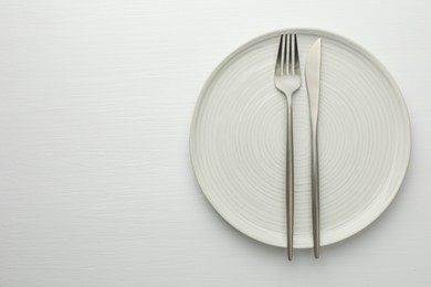Clean plate, fork and knife on white table, top view. Space for text