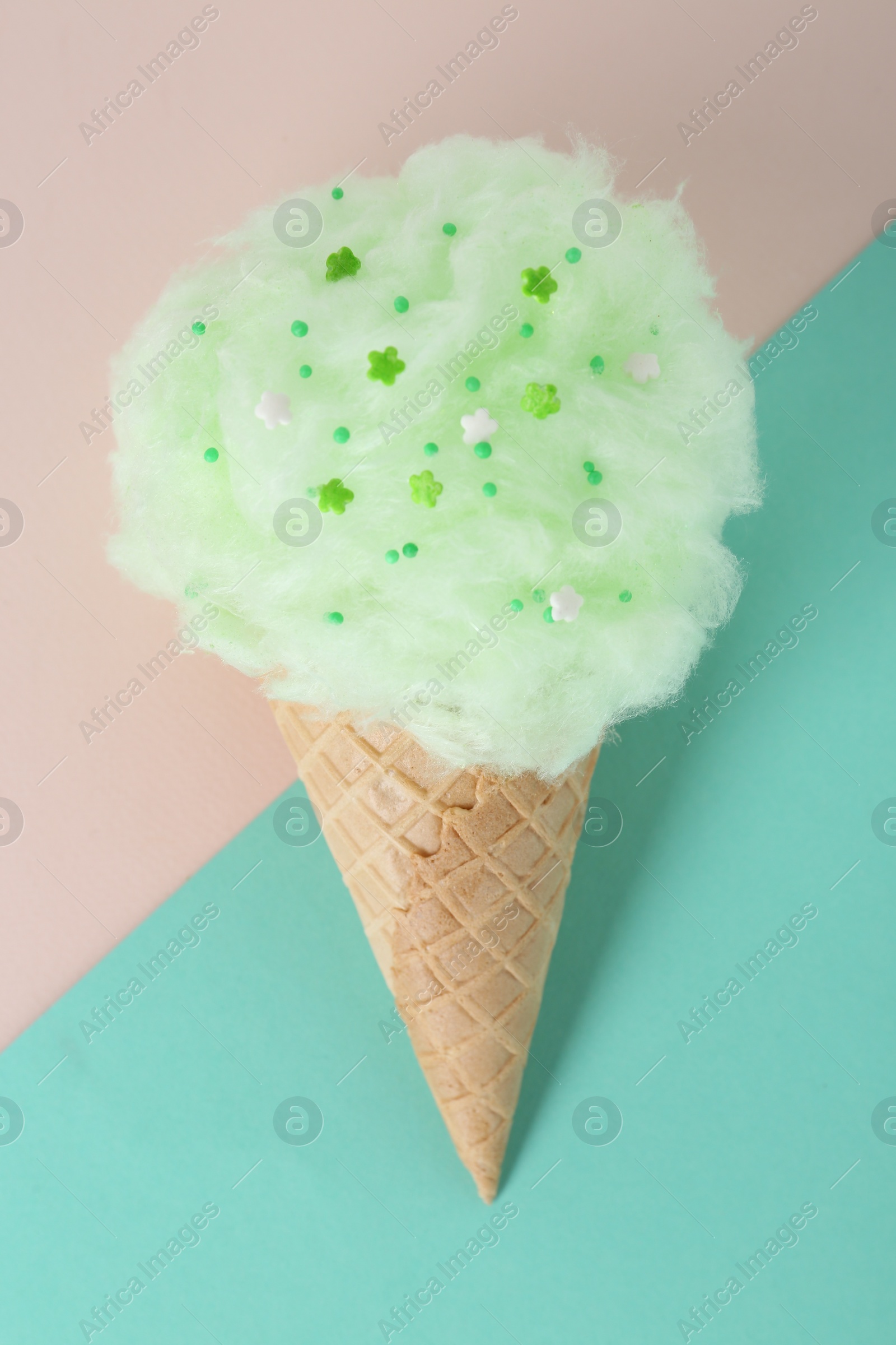 Photo of Sweet cotton candy in waffle cone on color background, top view