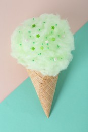 Sweet cotton candy in waffle cone on color background, top view