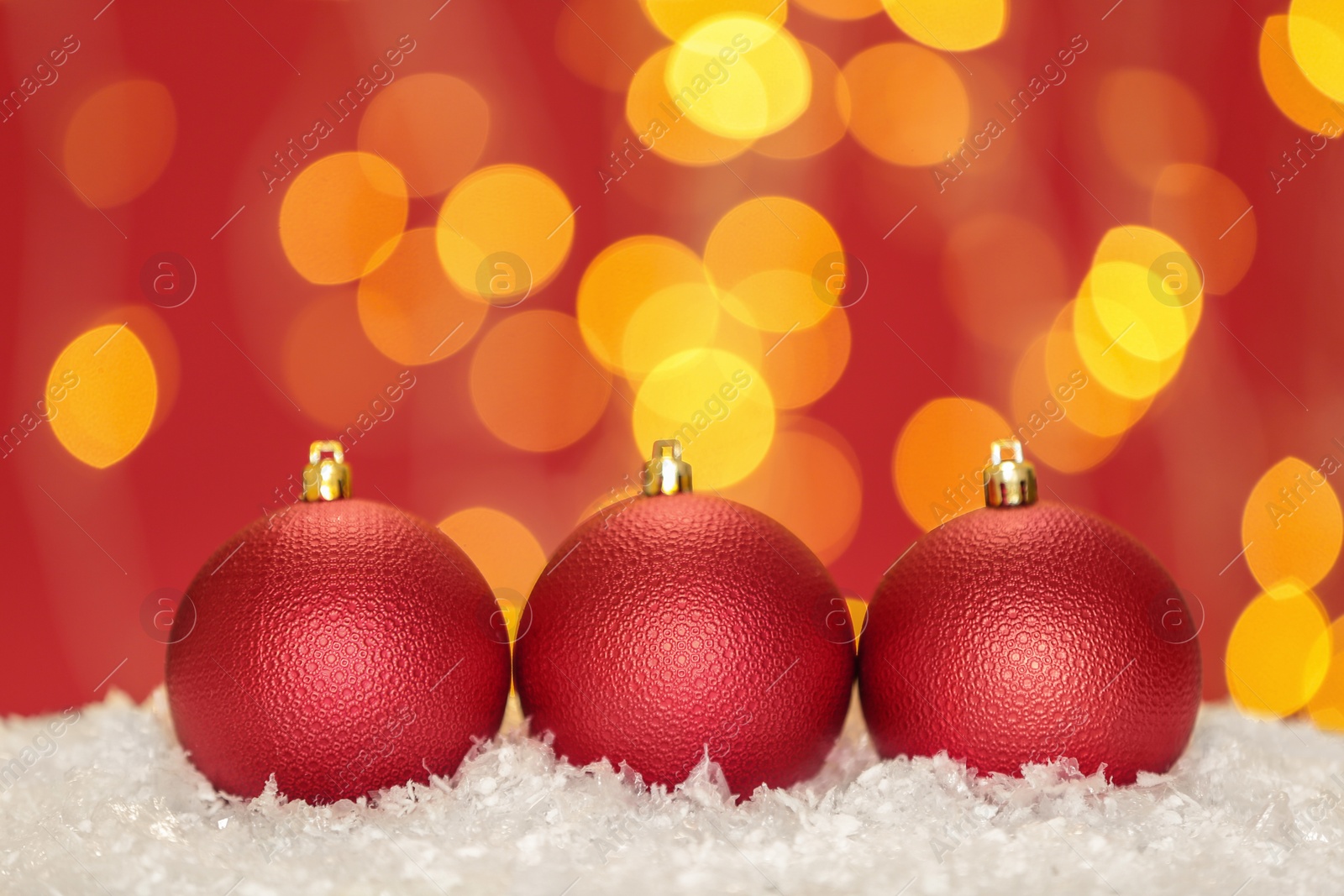 Photo of Beautiful red Christmas balls on snow against blurred festive lights, space for text