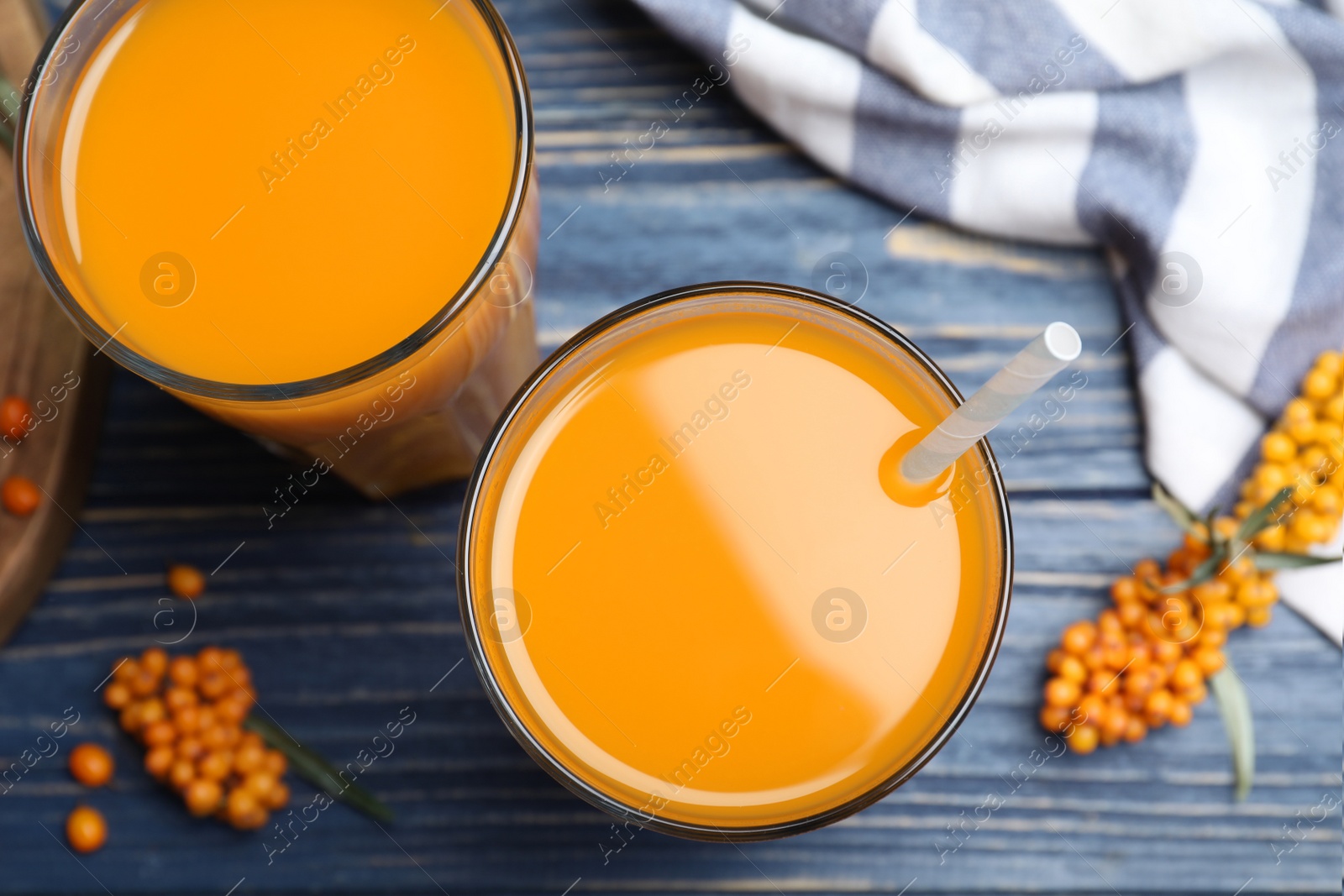 Photo of Sea buckthorn juice and fresh berries on blue wooden table, top view