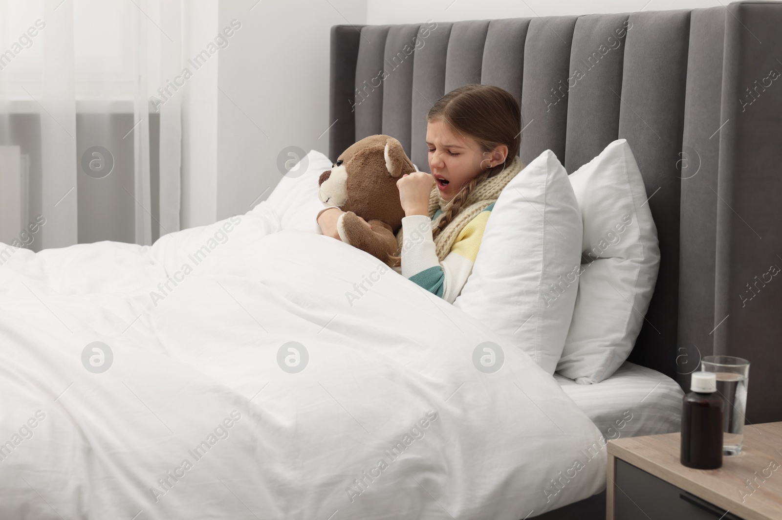 Photo of Sick girl with teddy bear coughing on bed at home