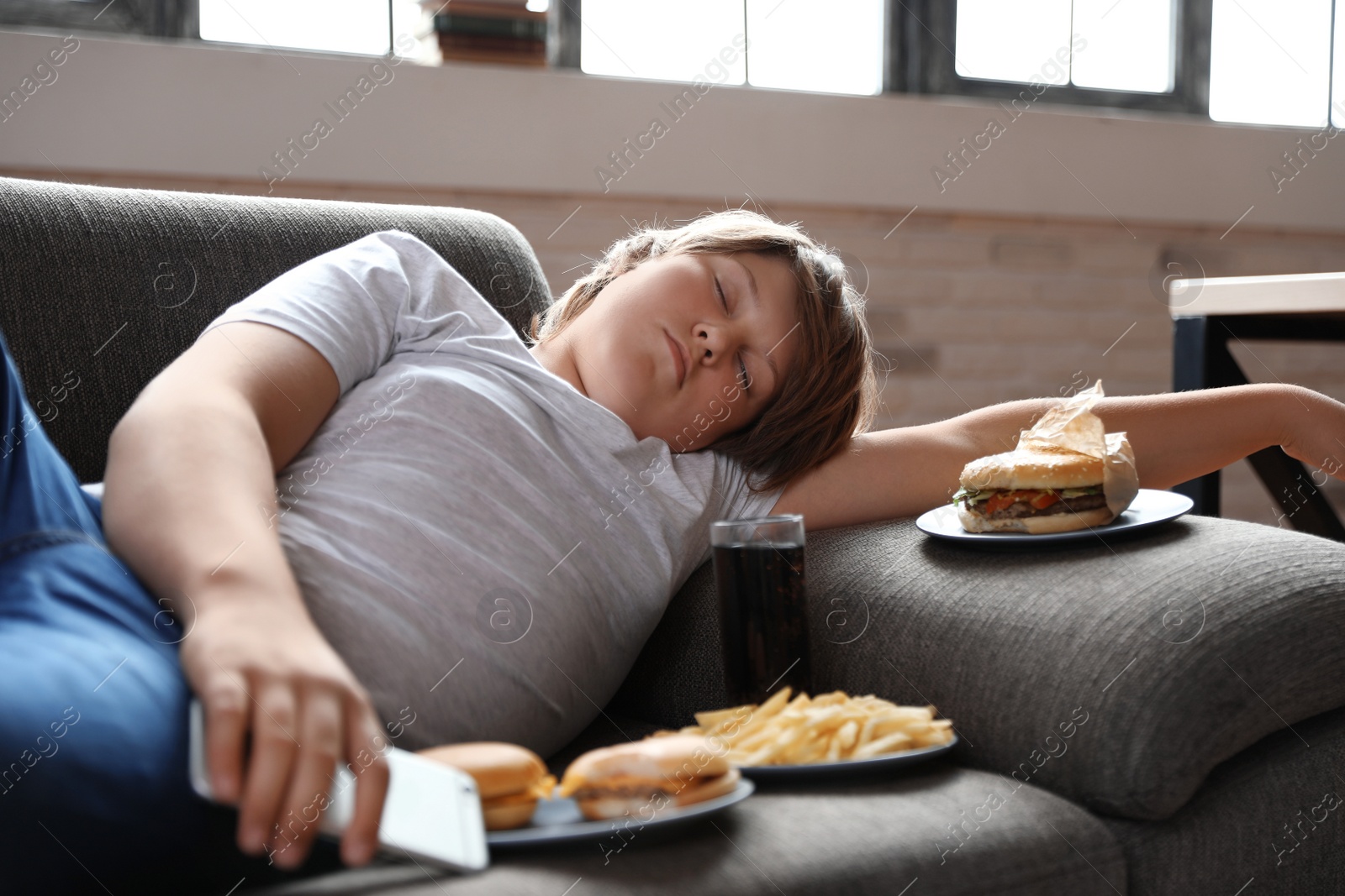 Photo of Overweight boy sleeping on sofa surrounded by fast food