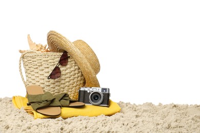 Stylish bag with beach accessories and camera on sand against white background