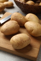 Photo of Many fresh potatoes, board and knife on grey table, closeup