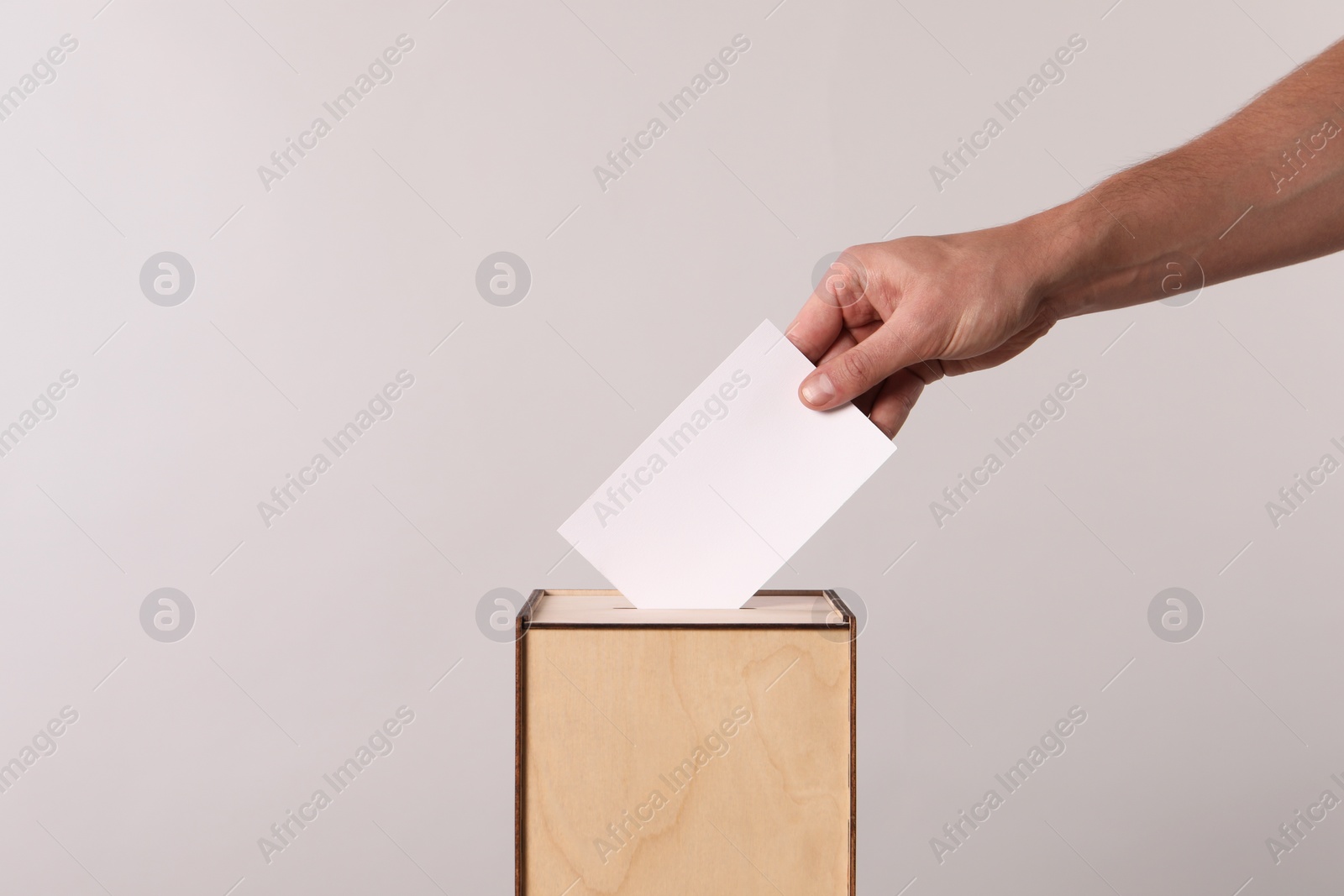 Photo of Man putting his vote into ballot box on light grey background, closeup