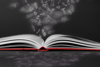 Image of Open book with flying letters on black background. Dyslexia concept