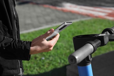 Photo of Man using smartphone to pay and unblock rental electric scooter outdoors, closeup