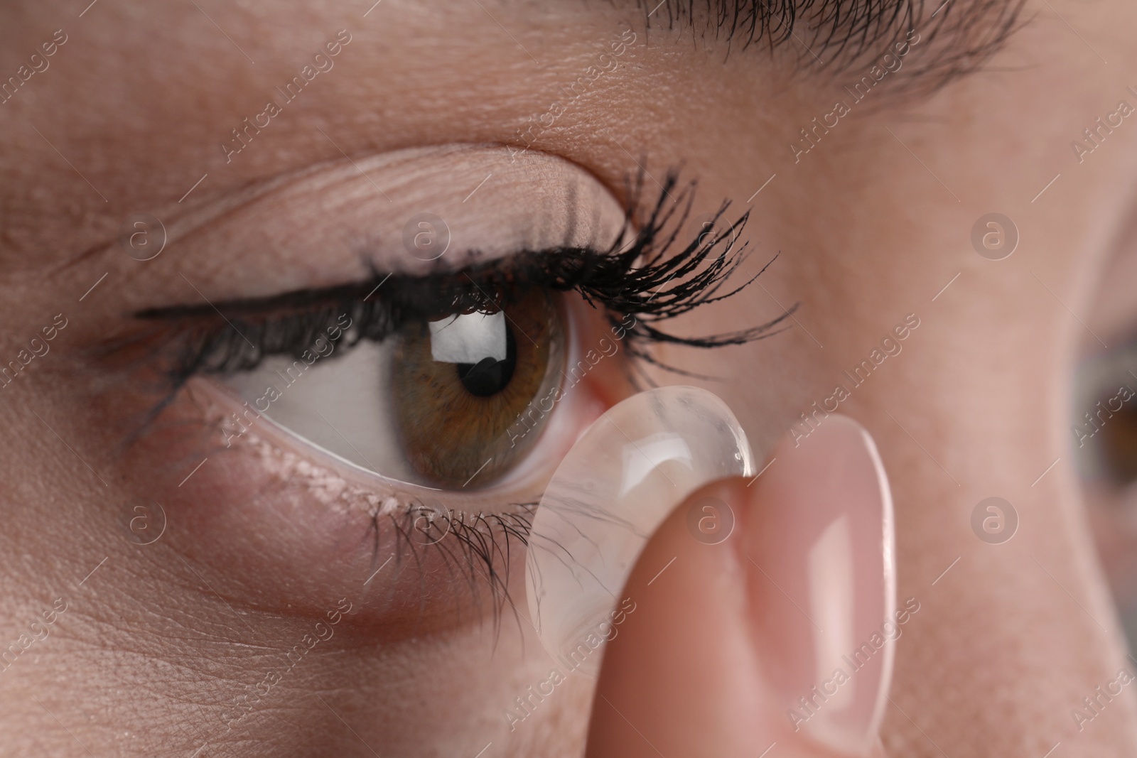 Photo of Closeup view of young woman putting contact lens in her eye