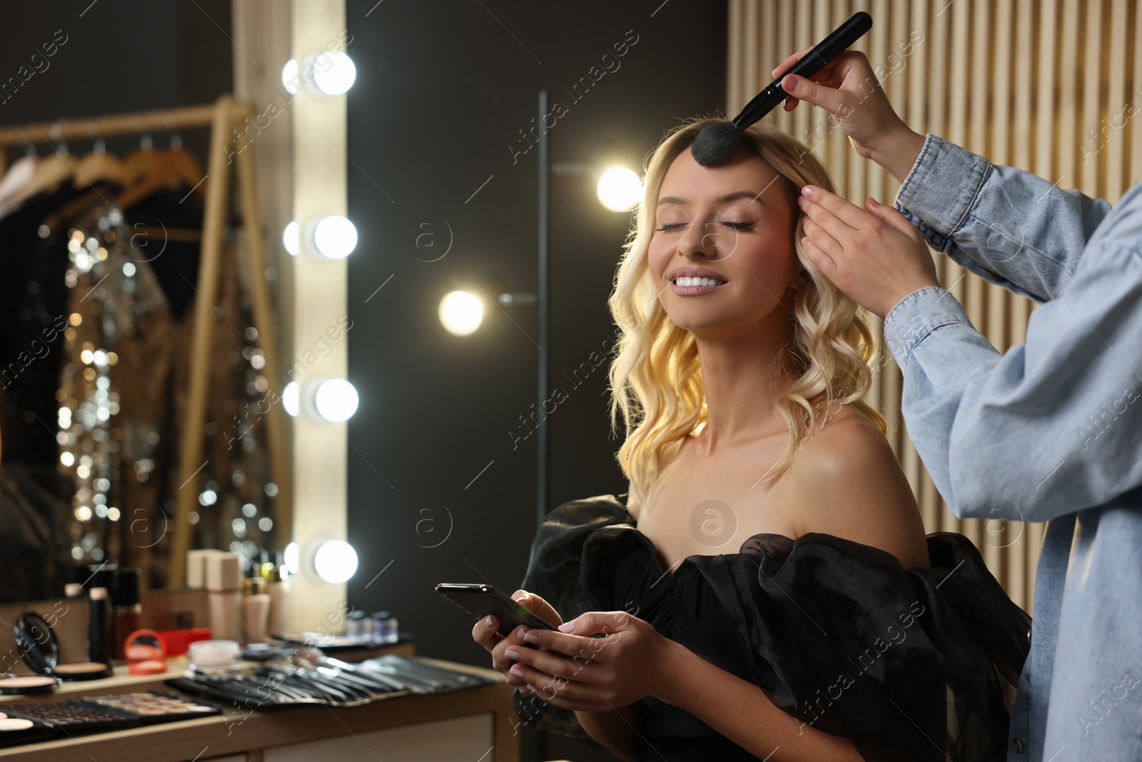 Photo of Makeup artist working with beautiful woman in dressing room, closeup