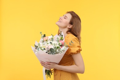 Happy woman with bouquet of beautiful flowers on yellow background