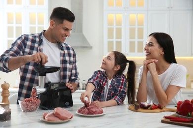 Photo of Happy family making dinner together in kitchen, daughter helping her father while he using modern meat grinder