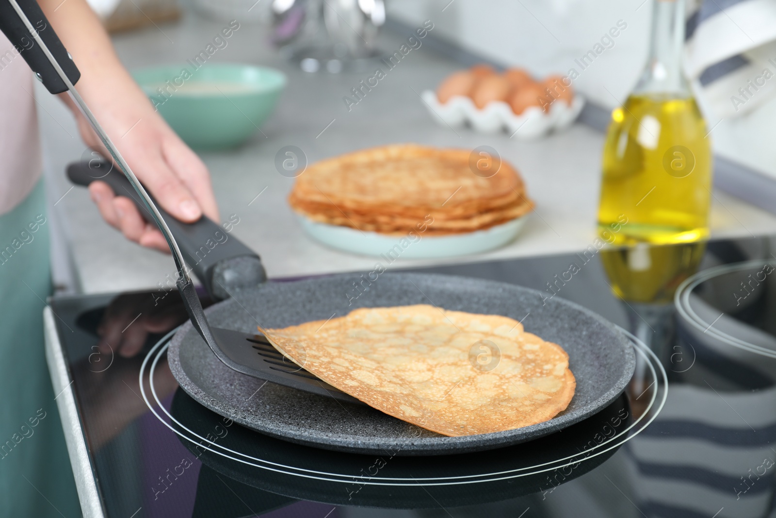 Photo of Woman cooking delicious thin pancakes on induction stove, closeup