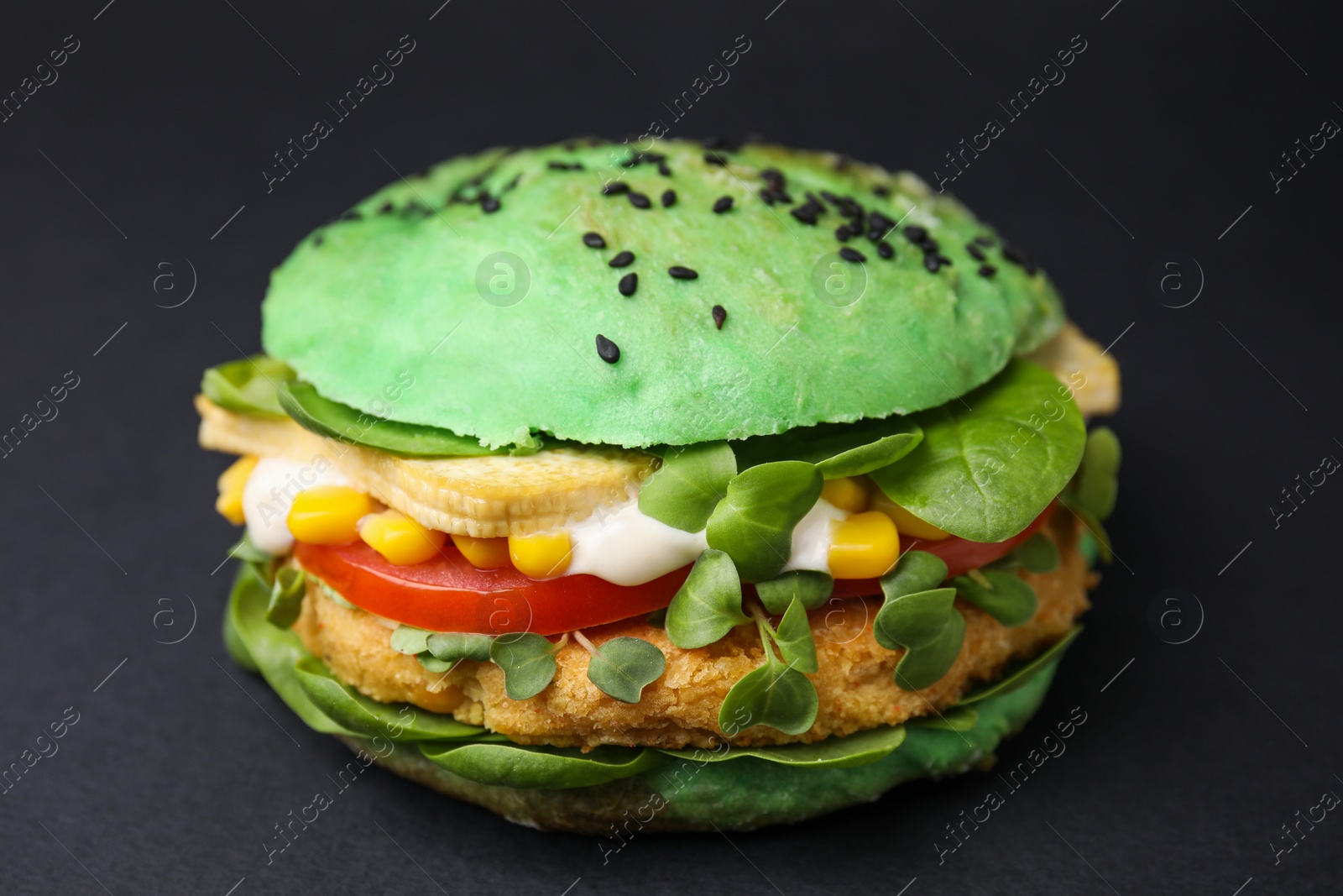 Photo of Tasty green vegan burger with vegetables, patty and microgreens on black background, closeup