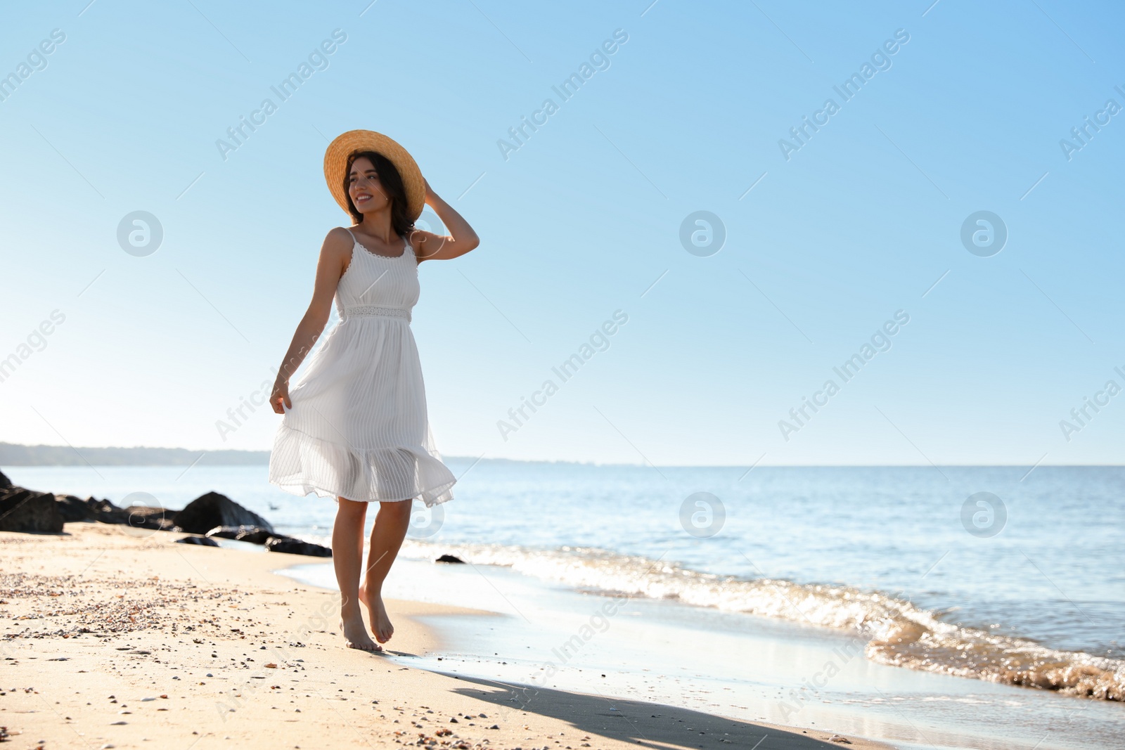 Photo of Happy young woman with hat walking on beach near sea. Space for text