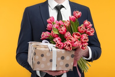 Man with beautiful bouquet and present on orange background, closeup