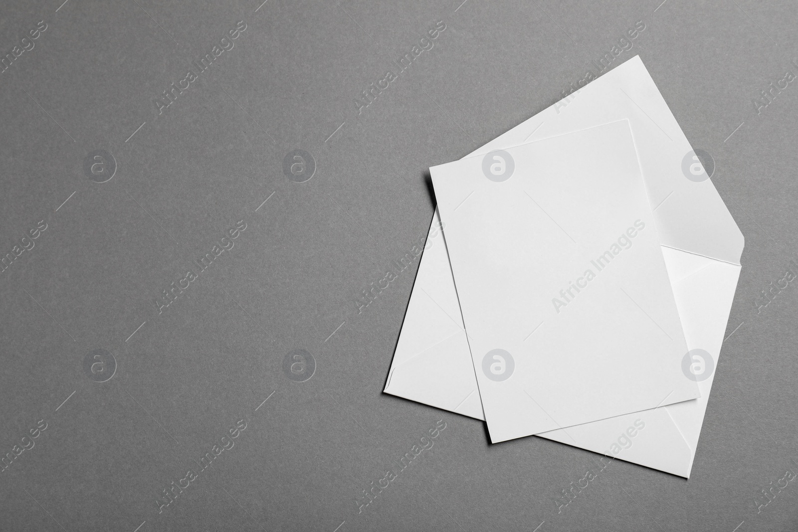 Photo of Blank sheet of paper and letter envelope on grey background, top view. Space for text