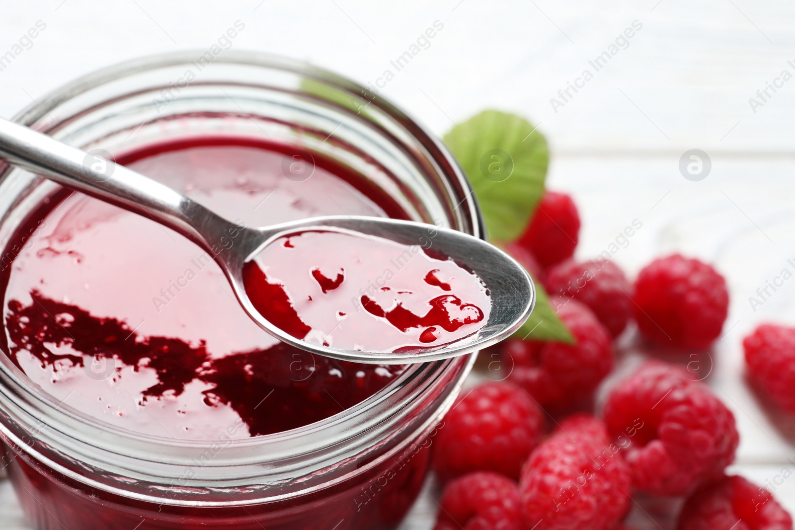 Image of Sweet raspberry jam and fresh berries on white wooden table, closeup