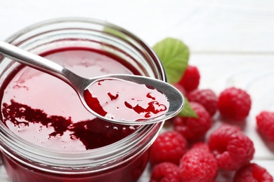 Image of Sweet raspberry jam and fresh berries on white wooden table, closeup