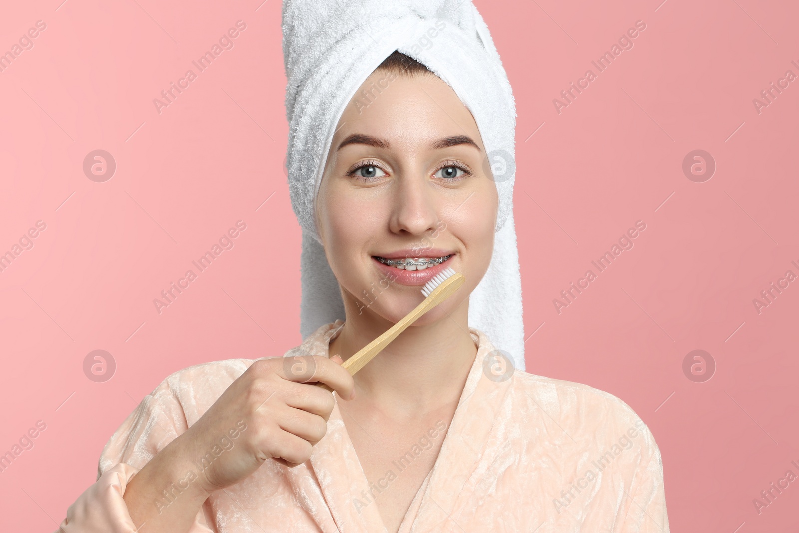 Photo of Smiling woman with dental braces cleaning teeth on pink background