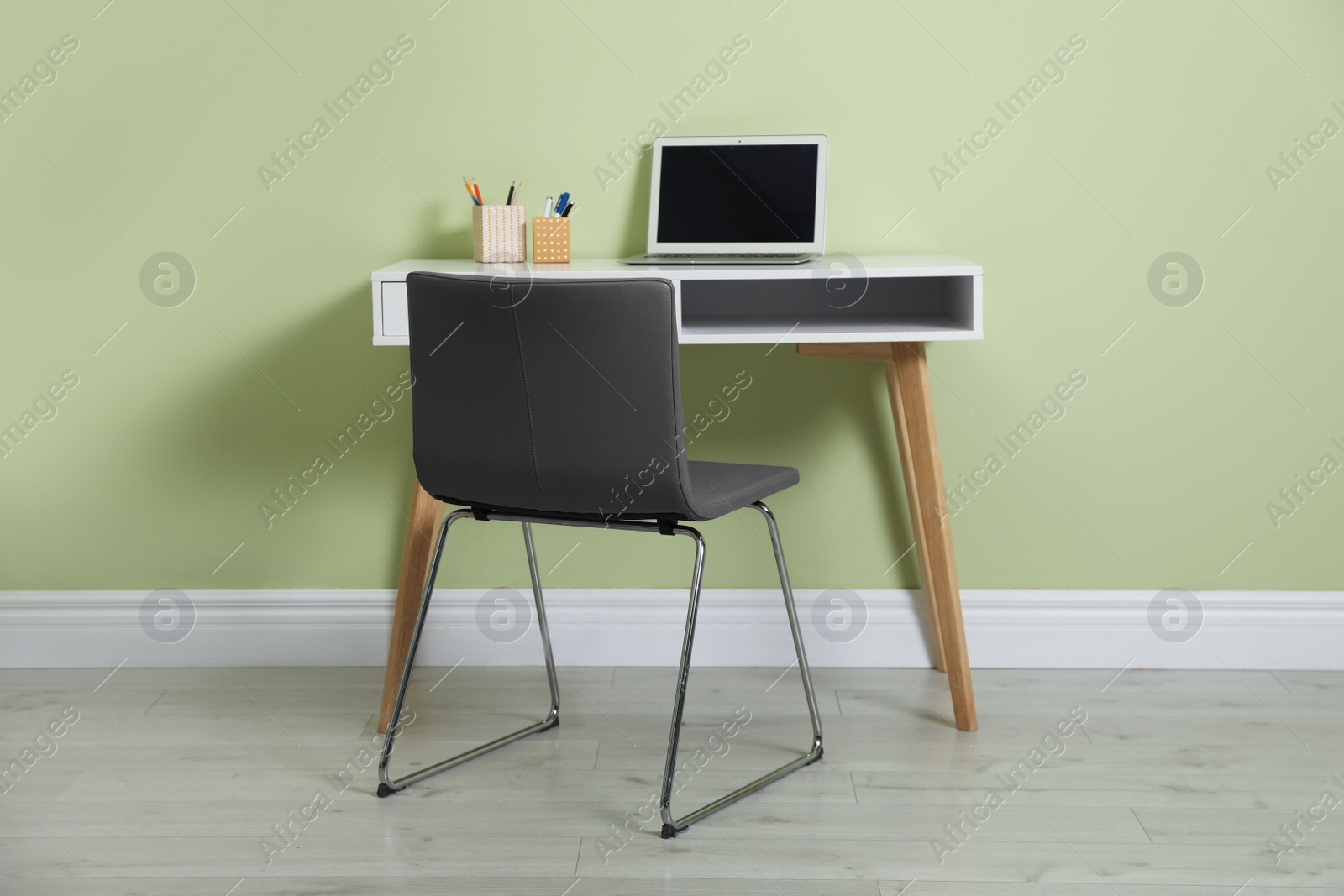 Photo of Stylish workplace with laptop and comfortable chair near green wall indoors. Interior design